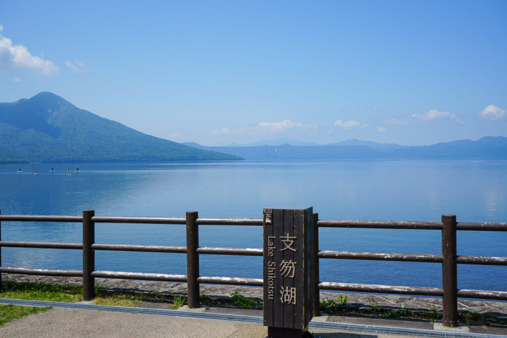 支笏湖の標識とSUPが浮かぶ青い湖面と山並み