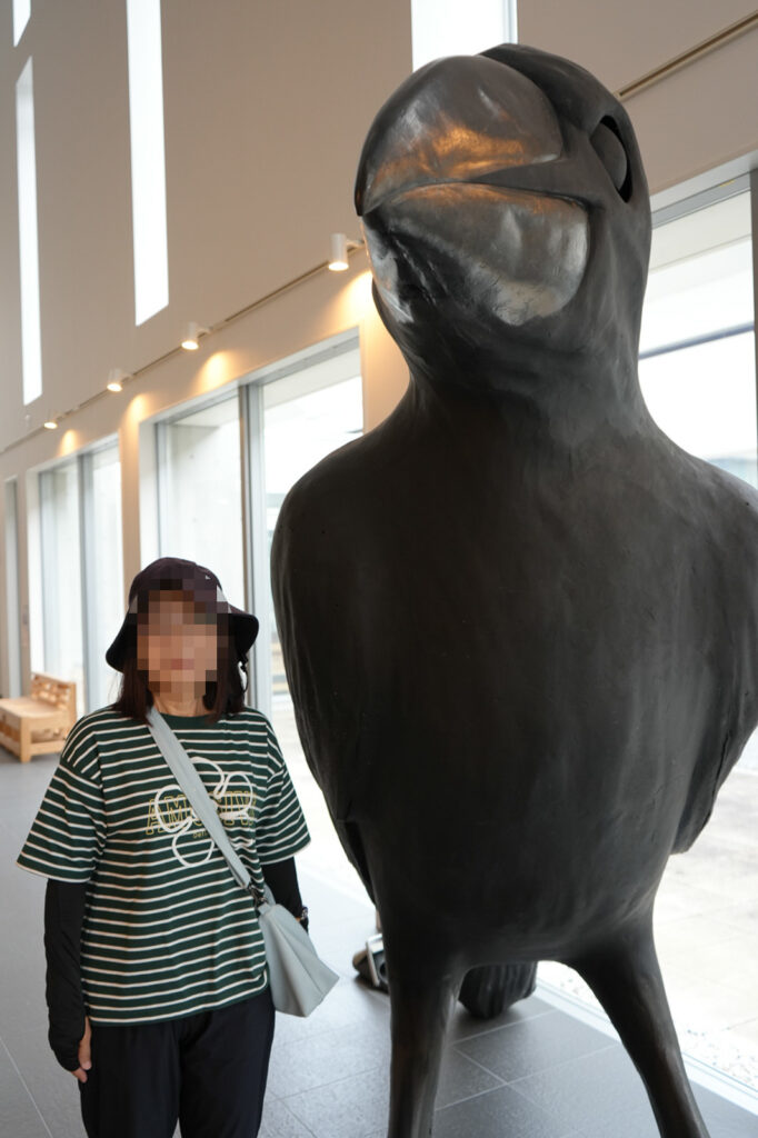 ミュージアムエントランスに立つ大型のカラス彫刻と見学者