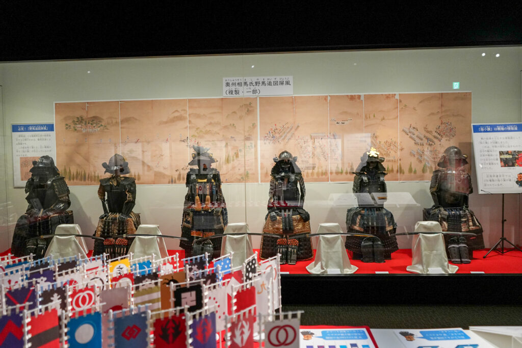 野馬追図屏風前に並ぶ甲冑5体と指物旗の模型