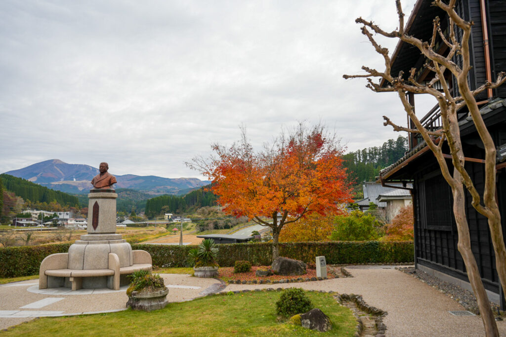 紅葉の木と山を背景に立つ北里柴三郎の胸像