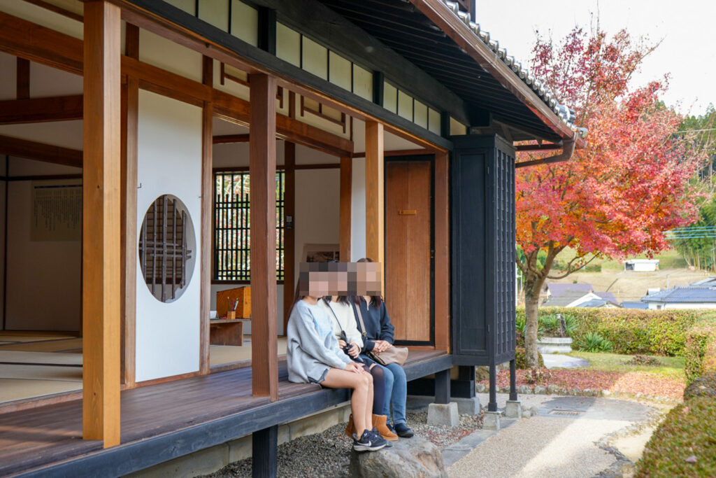 北里柴三郎記念館の縁側に並んで座る3人と紅葉の木