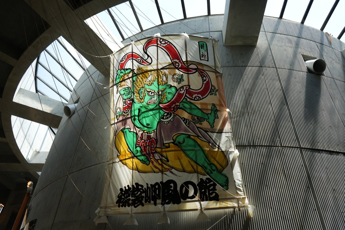 近代的な吹き抜け建物内に展示された風神の絵が描かれた大型日本凧