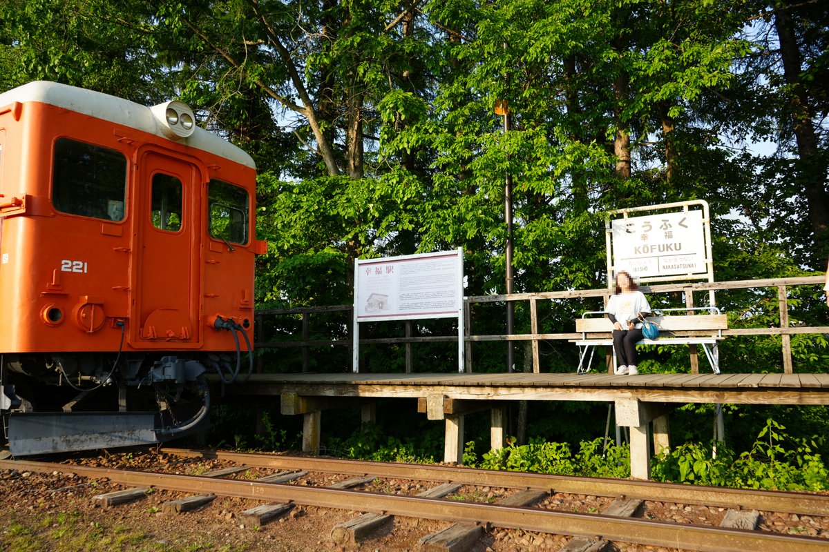 北海道帯広・幸福駅のホームに停車するオレンジ色のディーゼル車両と木製プラットフォームに座る女性