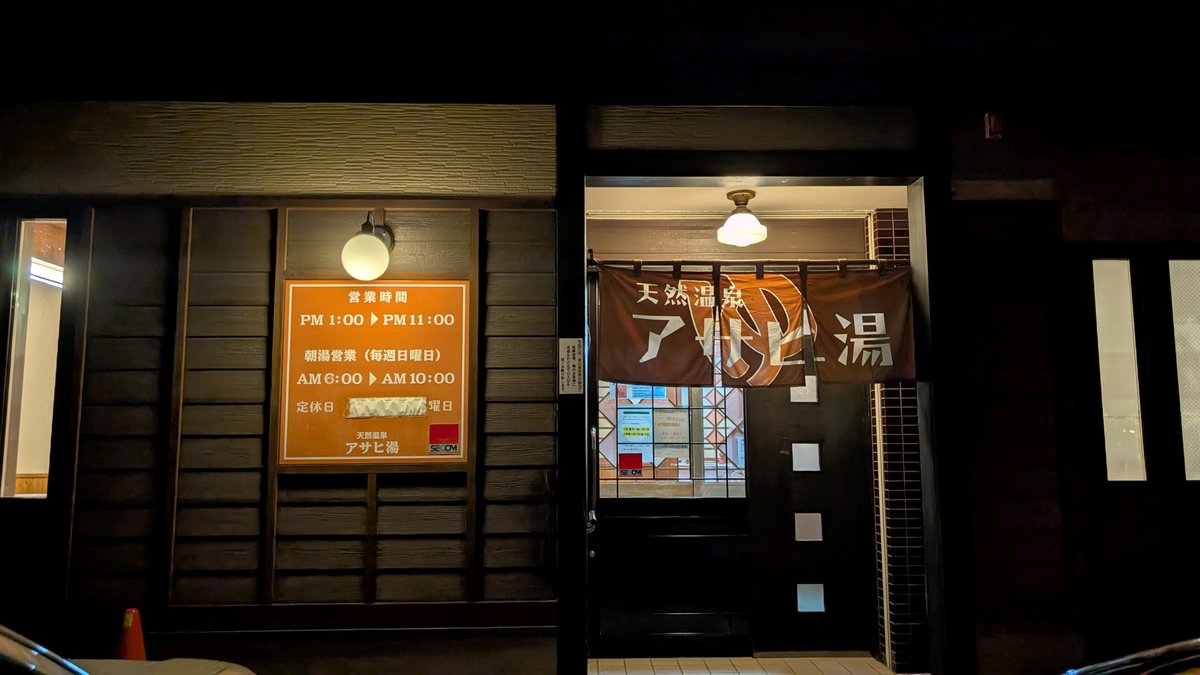 天然温泉アサヒ湯の夜の外観。暖簾と営業時間の看板が掲げられた入口