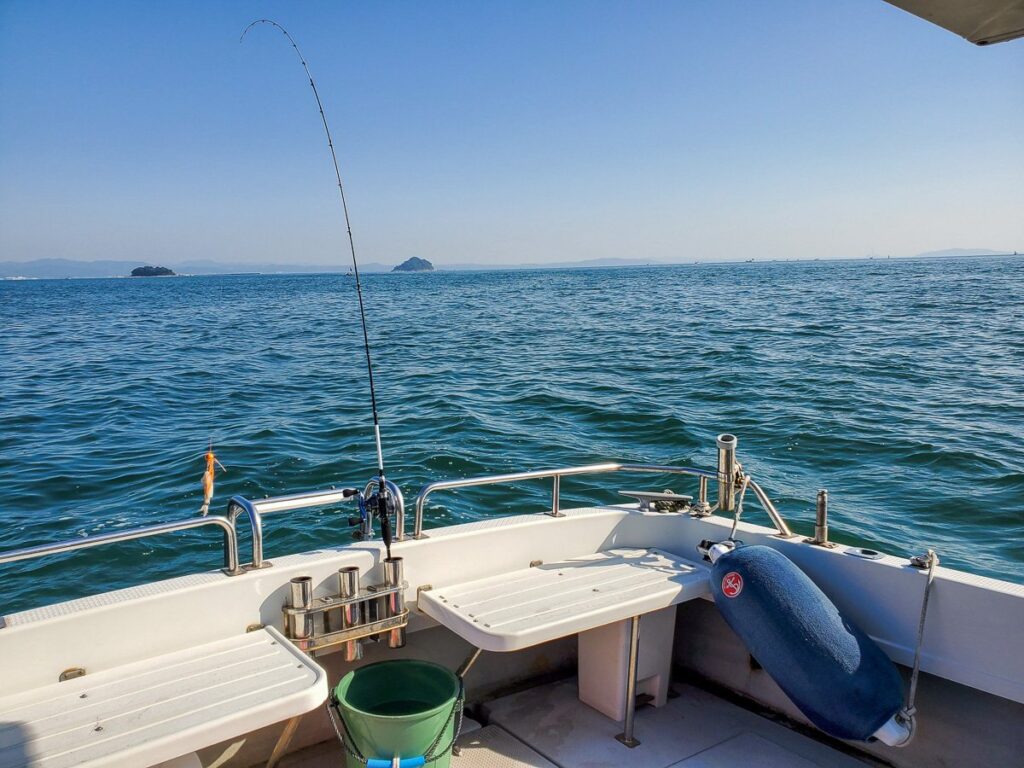 釣り船の船尾デッキから見た青い海と釣り竿、遠方に浮かぶ島々