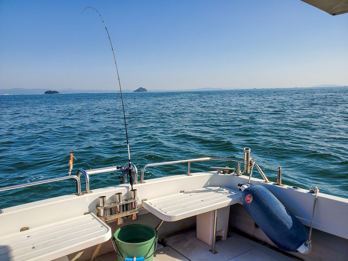 釣り船の船尾デッキから見た青い海と釣り竿、遠方に浮かぶ島々