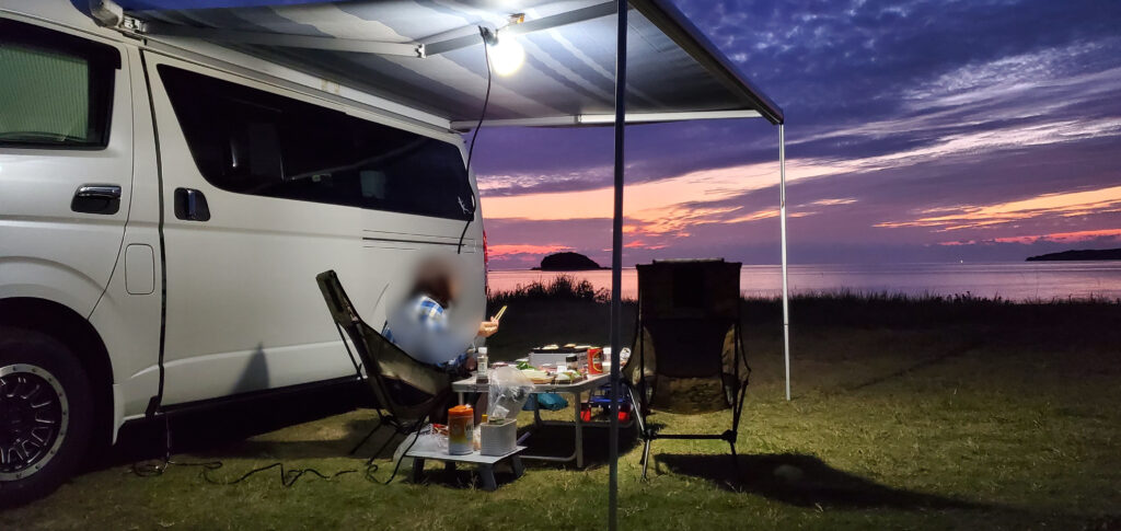 夕暮れの海辺でオーニングを張り夕食を楽しむハイエース